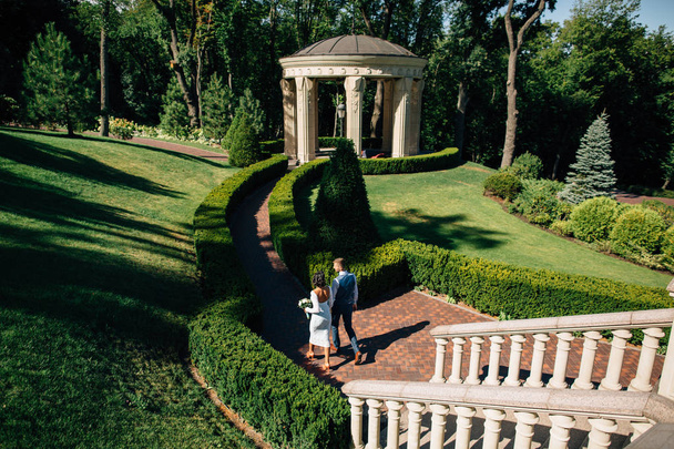 Newlyweds walking in garden of luxury mansion on wedding day - Fotó, kép