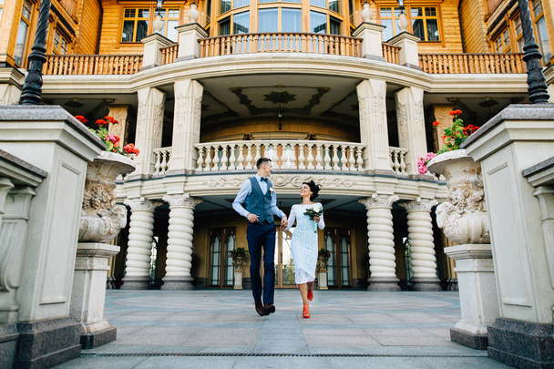 Happy newlyweds running on the background of luxury mansion on wedding day - Foto, Imagen