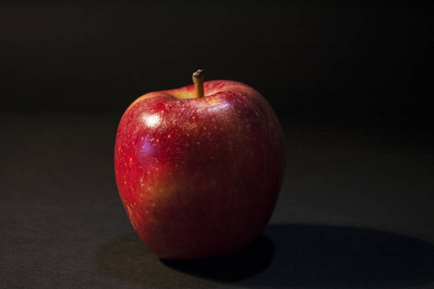 Ένα όμορφο ζουμερό κόκκινο μήλο. Σε μαύρο φόντο. Ένα μήλο στη φωτογραφία. Φωτεινή φωτογραφία. - Φωτογραφία, εικόνα
