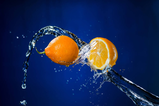 two halves of orange and splash of water on blue background - Valokuva, kuva