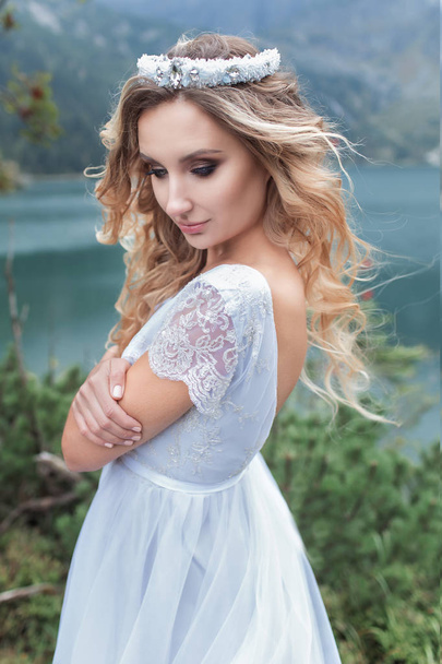 beautiful gentle girl bride in the air fairy blue wedding dress with luxurious curls in the mountains near the lake with a crown utterly - 写真・画像