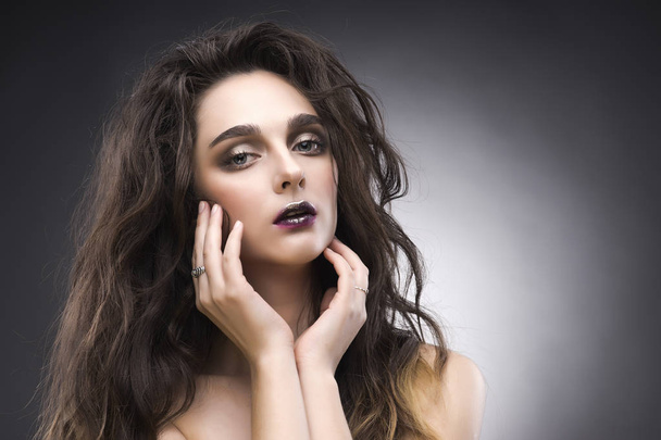 beauty portrait of the young woman in a with a vanguard make-up and a flowing hair on a gray background - Photo, image