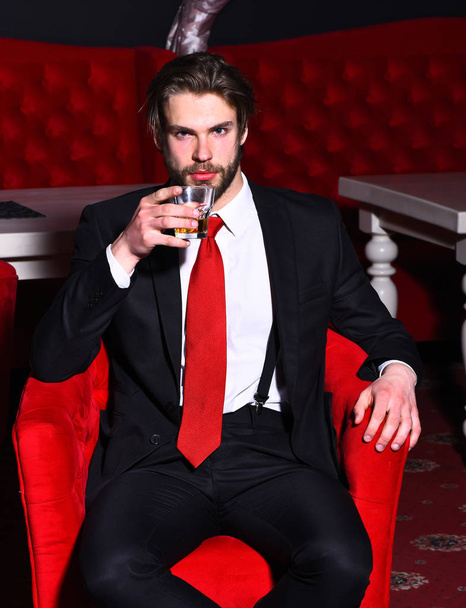 bearded man, businessman holding glass of whiskey in red chair - Φωτογραφία, εικόνα