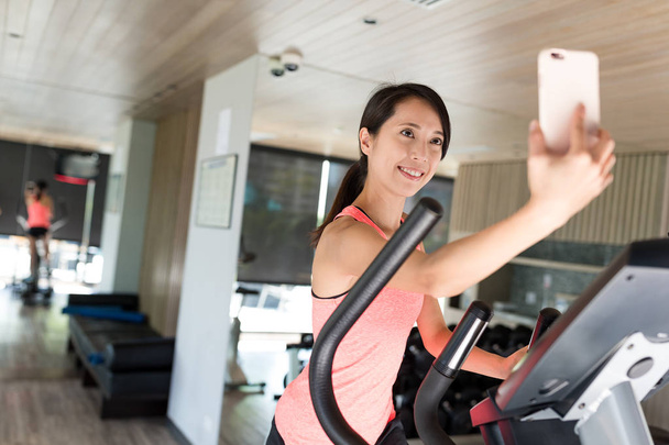 Vrouw training op elliptische machine en nemen selfie - Foto, afbeelding