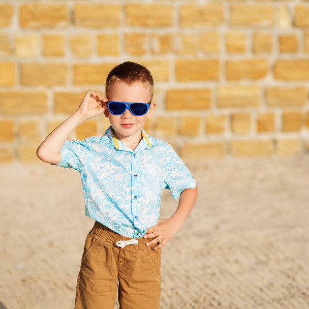 kisfiú a sárga téglák ellen kék tükör napszemüveget visel - Fotó, kép