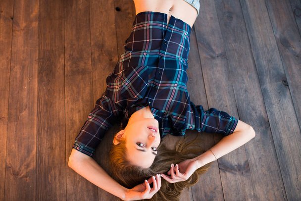 Beautiful brunette girl lying on the wooden floor. Studio shot - Foto, Imagen