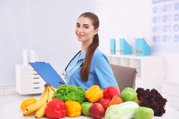 Young female nutritionist with vegetables and fruits in her office - Фото, зображення