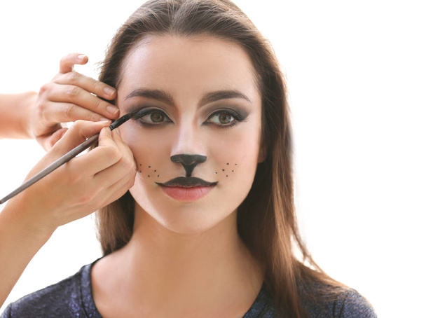Visagiste applying cat makeup onto face of beautiful young woman in salon - Φωτογραφία, εικόνα