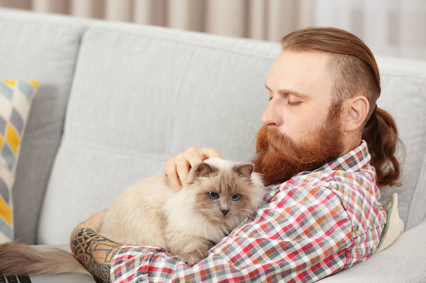 Young bearded man with fluffy cat sitting on sofa - Fotoğraf, Görsel