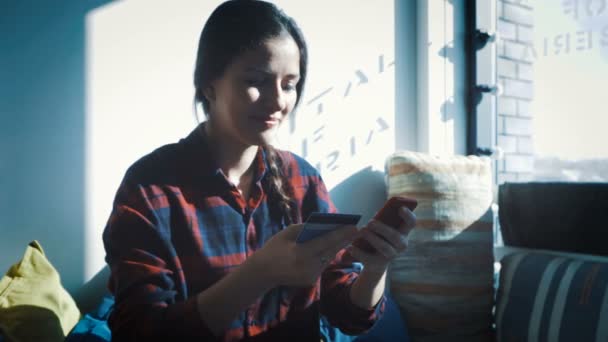 Smiling young woman sitting at table using touchpad and holding credit card in her hand - Záběry, video
