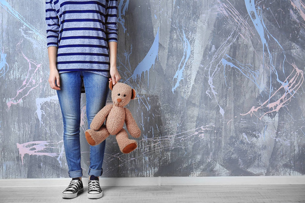 Little girl standing with toy bear on color wall background - Zdjęcie, obraz