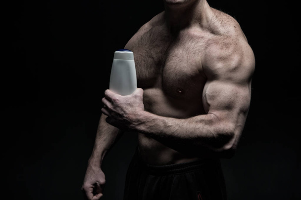 handsome bodybuilder man with muscular body holds shampoo bottle - Photo, image