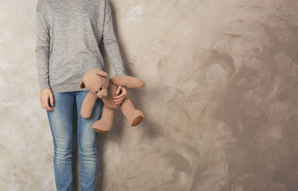 Little girl standing with toy bear on color wall background - Fotó, kép