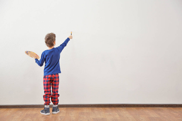 Cute little boy painting on wall in empty room - Фото, зображення