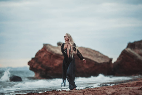 Young woman in long transparent black dress among beach and sea. - Fotó, kép