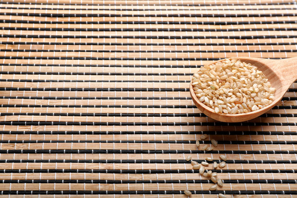 Rice in wooden spoon on wicker mat  - Φωτογραφία, εικόνα