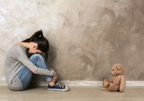 Little girl sitting with toy bear on color wall background - Foto, Imagen