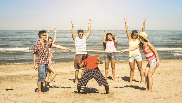 multiracial happy friends group having fun together with limbo game at beach - Sommerfreude und Freundschaftskonzept mit jungen multiethnischen Menschen, die in den Frühjahrsferien spielen - Retro-Vintage-Filter - Foto, Bild