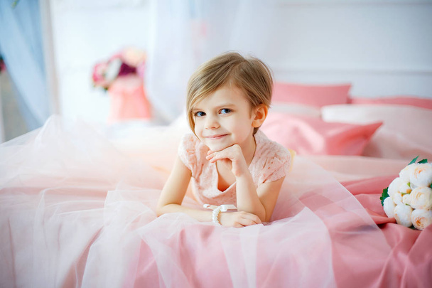 Маленька гарна дівчинка в сукні лежить на ліжку з квітами
 - Фото, зображення