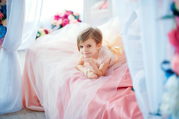 Little nice girl in dress lying on bed with flowers - Foto, afbeelding