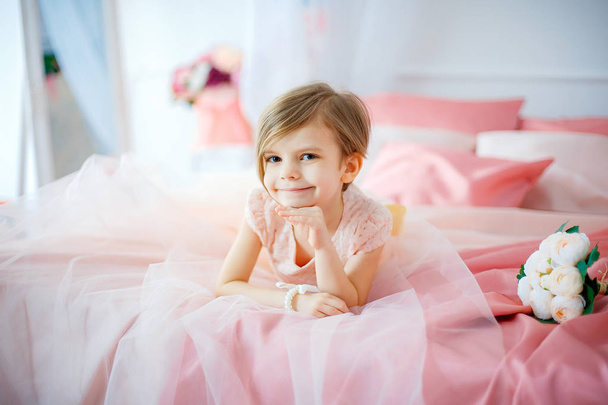 Little nice girl in dress lying on bed with flowers - Photo, Image