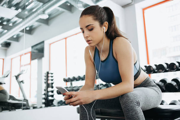 Young woman with earphones listening to music after hard workout in gym. - Fotó, kép