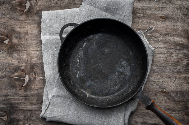 Sartén vacía de hierro fundido negro sobre una servilleta textil
 - Foto, imagen