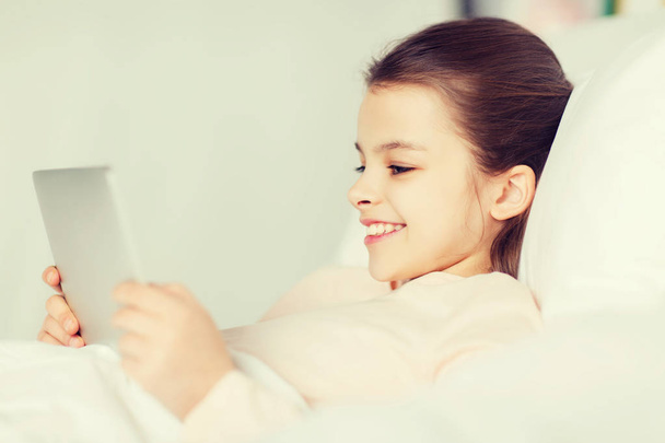 happy girl lying in bed with tablet pc at home - Фото, изображение