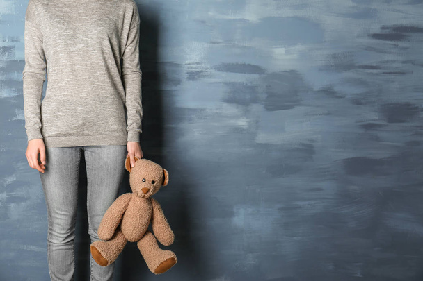 Little girl standing with toy bear on blue background - Foto, imagen