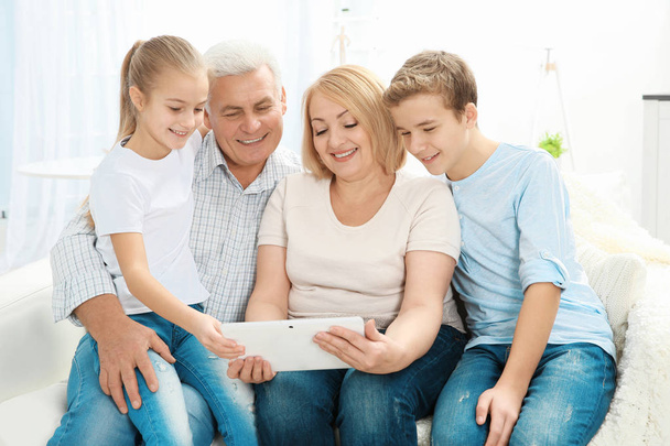 Cute children and their grandparents sitting on sofa with tablet computer - Фото, изображение