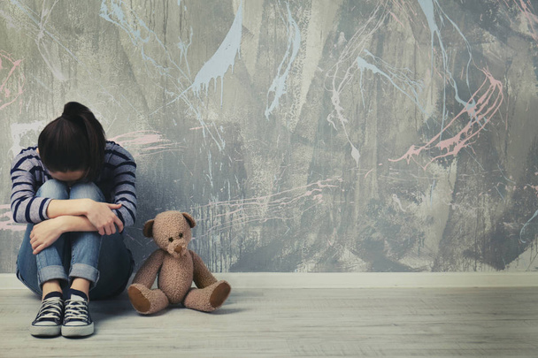 Little girl sitting with toy bear on color wall background - Foto, Bild