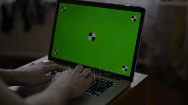 A man types on a laptop on his desk. Green screen for your custom screen content. - Materiał filmowy, wideo