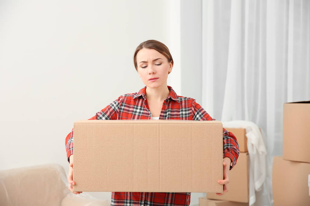 Young woman holding heavy box in room - Φωτογραφία, εικόνα