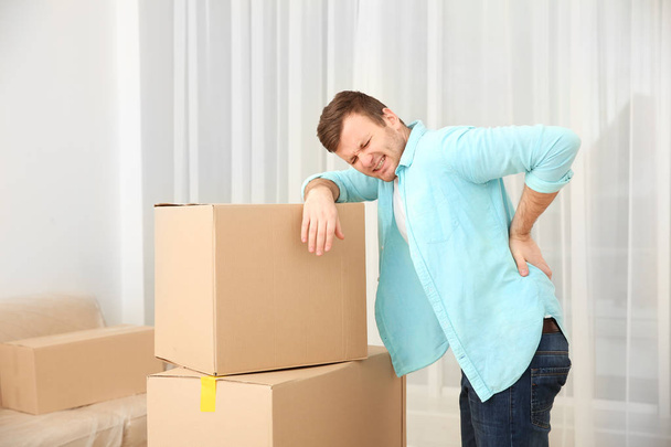 Young man suffering from pain after moving heavy box - 写真・画像