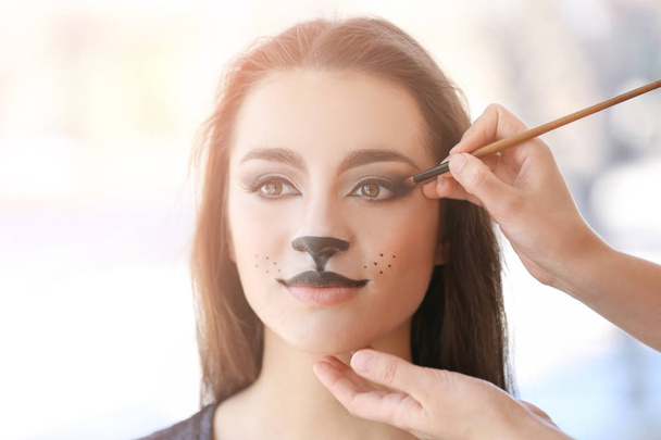 Visagiste applying cat makeup onto face of beautiful young woman in salon - Φωτογραφία, εικόνα