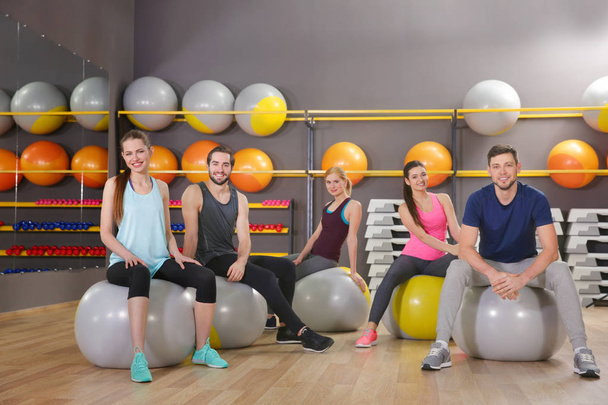 Young sporty people sitting on fit balls in gym - Photo, Image