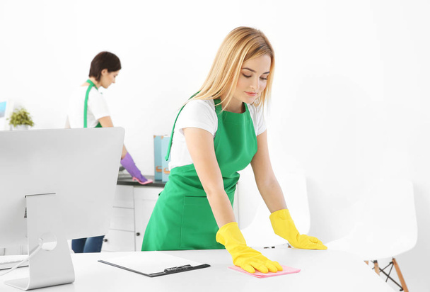 Young woman cleaning office table - Foto, imagen