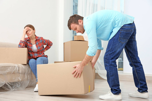 Couple suffering from ache while moving boxes in room - 写真・画像