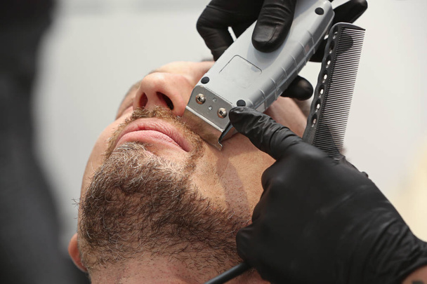Hairdresser shaving client in barbershop - Foto, afbeelding