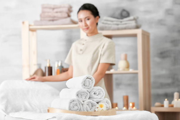 Wooden tray with pile of towels and female spa masseur on background - Photo, Image
