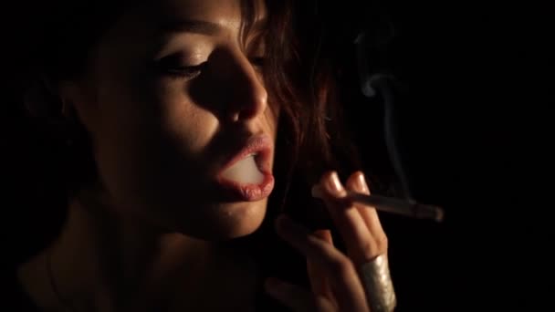 Beautiful young woman smoking a cigarette in the dark - Filmati, video