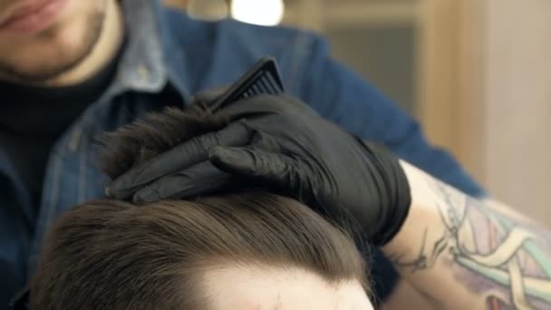 Master cuts hair and beard in the Barber shop. Black gloves with tattoos off of hands. close up - Video