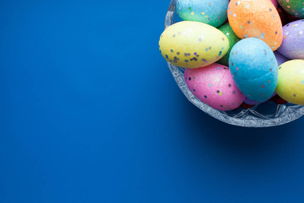 Huevos de Pascua en un plato de cristal sobre un fondo azul
, - Foto, Imagen
