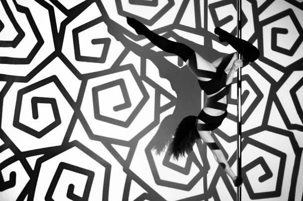 The girl on the pylon does the exercise against the background of black patterns. - Valokuva, kuva