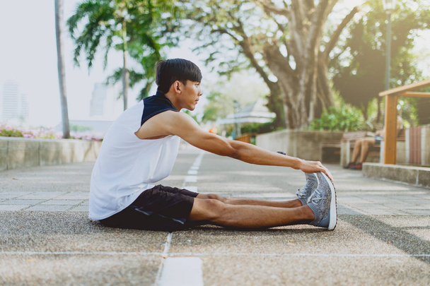Νεαρός άνδρας τέντωμα φορείς, προθέρμανση για τρέξιμο σε δημόσιο πάρκο. - Φωτογραφία, εικόνα