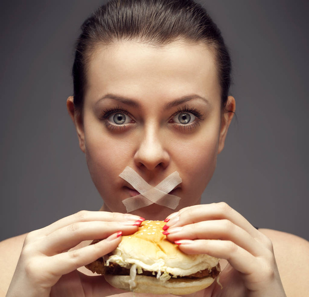 Diet concept: woman holding a burger with mouth sealed - Foto, imagen