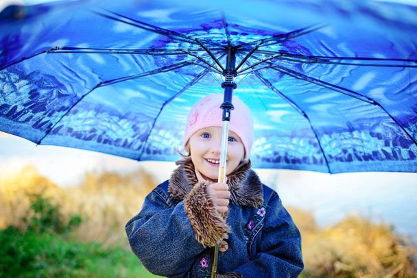 Kis lány és egy fiú esernyő játék az eső. A gyerekek játszanak szabadtéri az esős időjárás, ősszel. Őszi szórakozást a gyermekek számára. Kisgyermek gyerek esőkabát és bakancs sétálni a kertben. - Fotó, kép