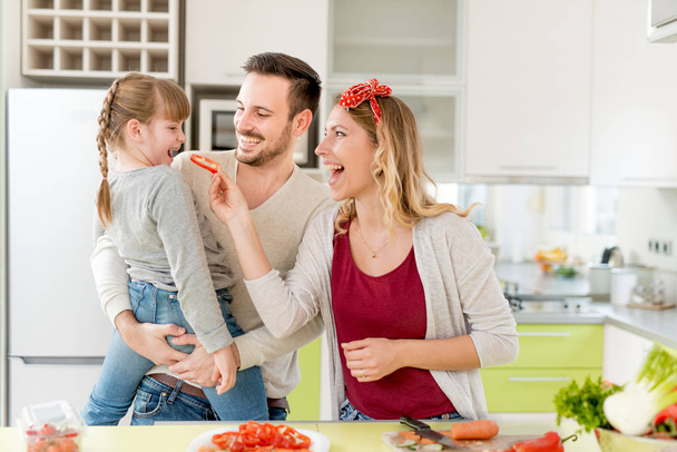 Onnellinen nuori perhe valmistelee lounasta keittiössä
  - Valokuva, kuva