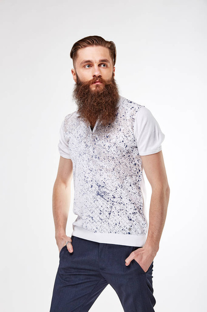 Young bearded man posing in studio in trendy white t shirt with print and blue chinos - Photo, image