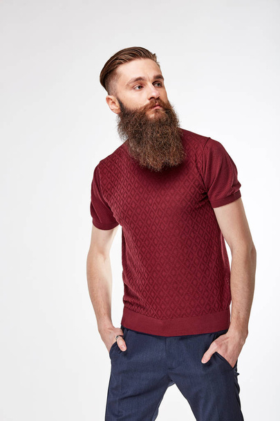 Young bearded man posing in studio in trendy dark red t shirt with stripes and blue chinos - Fotografie, Obrázek
